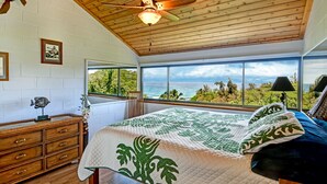 Une chambre avec un grand lit, un plafond en bois et une vue sur l’océan.