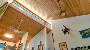 Une pièce avec un plafond en bois, un ventilateur de plafond, une décoration murale représentant une tortue et un tableau encadré.