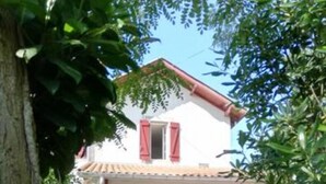 A two-story house with a tiled roof, a porch with outdoor furniture, and a bicycle parked outside. - Vacation in the heart of the Basque Country, swimming pool, quiet mountain views (Ossès)