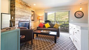 A living room with a fireplace, sofa, coffee table, and a view of the outdoors. - Acorn Chalet #2 - Walk to PC ski base! - 1BD (Park City)