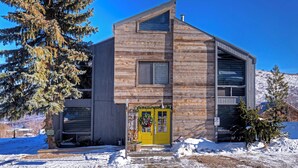 A modern log cabin with a yellow front door, a large window, and a garage. - Acorn Chalet #2 - Walk to PC ski base! - 1BD (Park City)