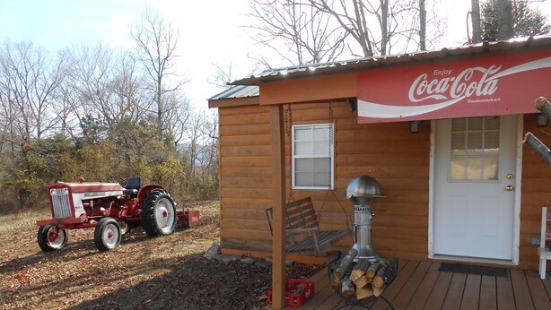 Een houten blokhut met een Coca-Cola bord, een barbecue en een tractor voor de deur.