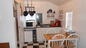 Een kleine keuken met een geruit vloertje, witte kastjes, een magnetron en een eettafel met stoelen.