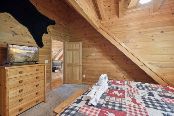Un dormitorio de cabaña de madera con una cama, un aparador y un televisor sobre él.