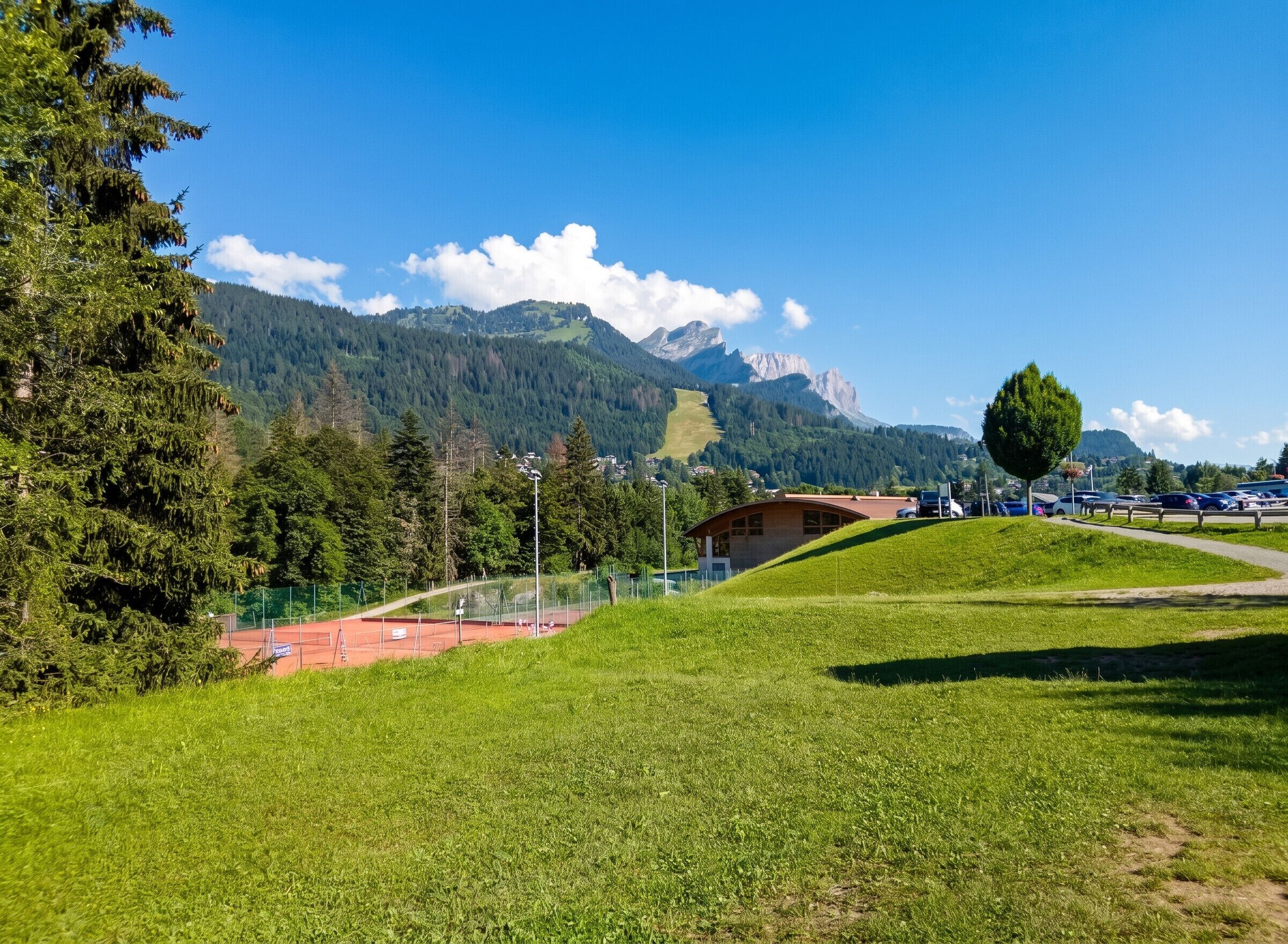 Een grasveld met een gebouw, een tennisbaan en bergen op de achtergrond.