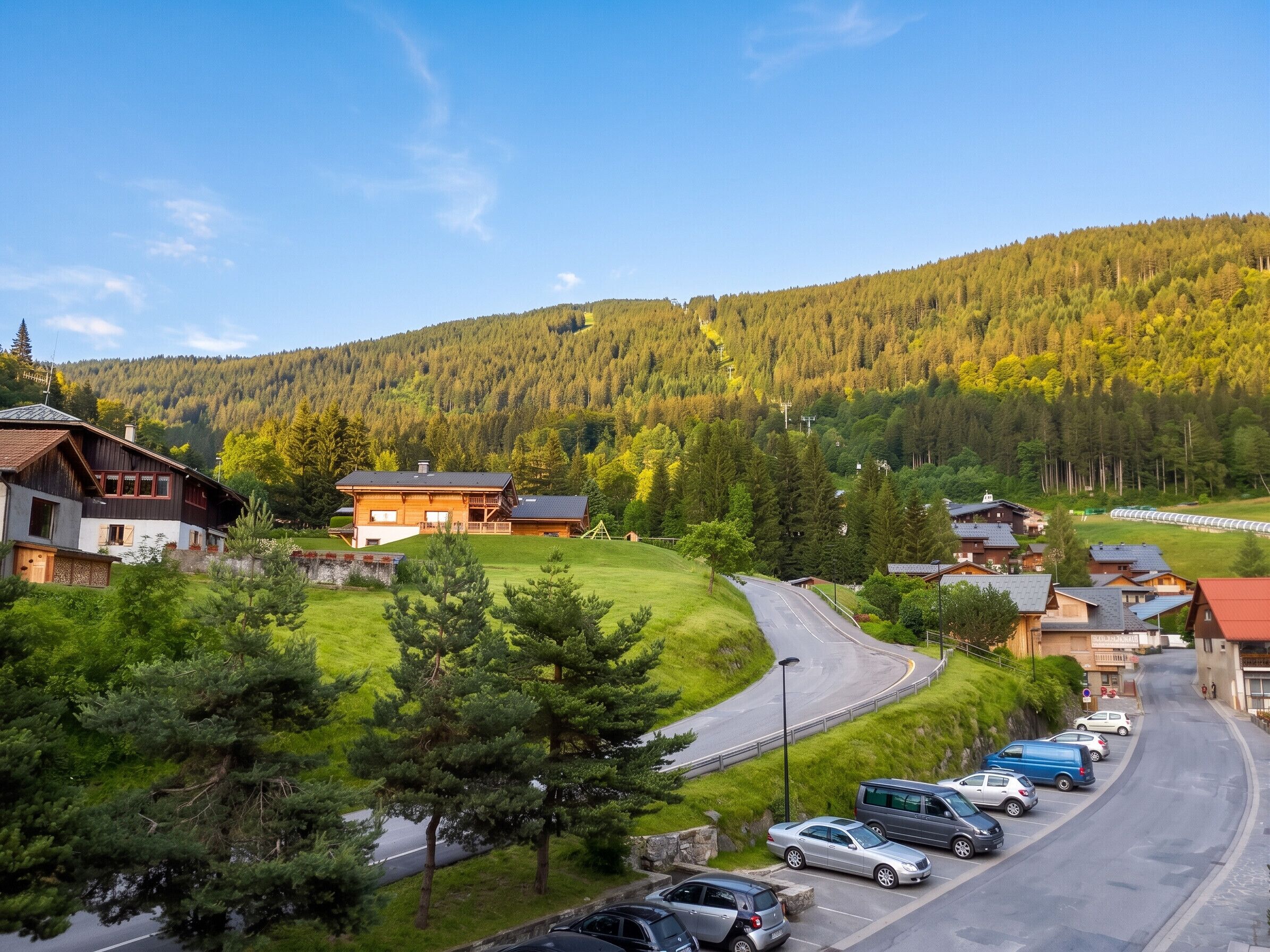 A mountain village with traditional wooden houses, a winding road, and a parking area.
