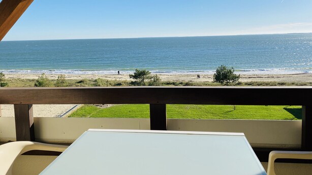 Une vue sur la plage depuis un espace abrité, équipé d’une table et de chaises.
