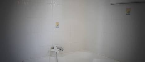 Een standaard wit bad met een handdouche, geplaatst tegen een effen betegelde muur.