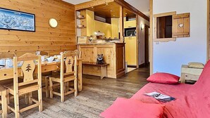 A cozy cabin interior with a dining area, kitchen, and a red sofa.