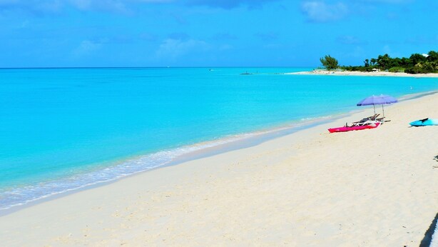A beach with clear turquoise water, a sandy shore, and a few beach umbrellas. - Spacious Villa for Families & Groups • Pool + Waterslide. Rent 4 or 5 Bedrooms (Providenciales)