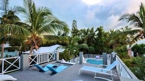 A rooftop pool area with lounge chairs and a swimming pool, surrounded by palm trees and greenery. - Spacious Villa for Families & Groups • Pool + Waterslide. Rent 4 or 5 Bedrooms (Providenciales)