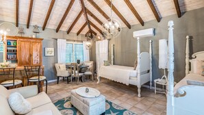 A spacious room with a high ceiling, a four-poster bed, a dining area with a table and chairs, and a cozy seating area with a sofa and ottoman. - Spacious Villa for Families & Groups • Pool + Waterslide. Rent 4 or 5 Bedrooms (Providenciales)
