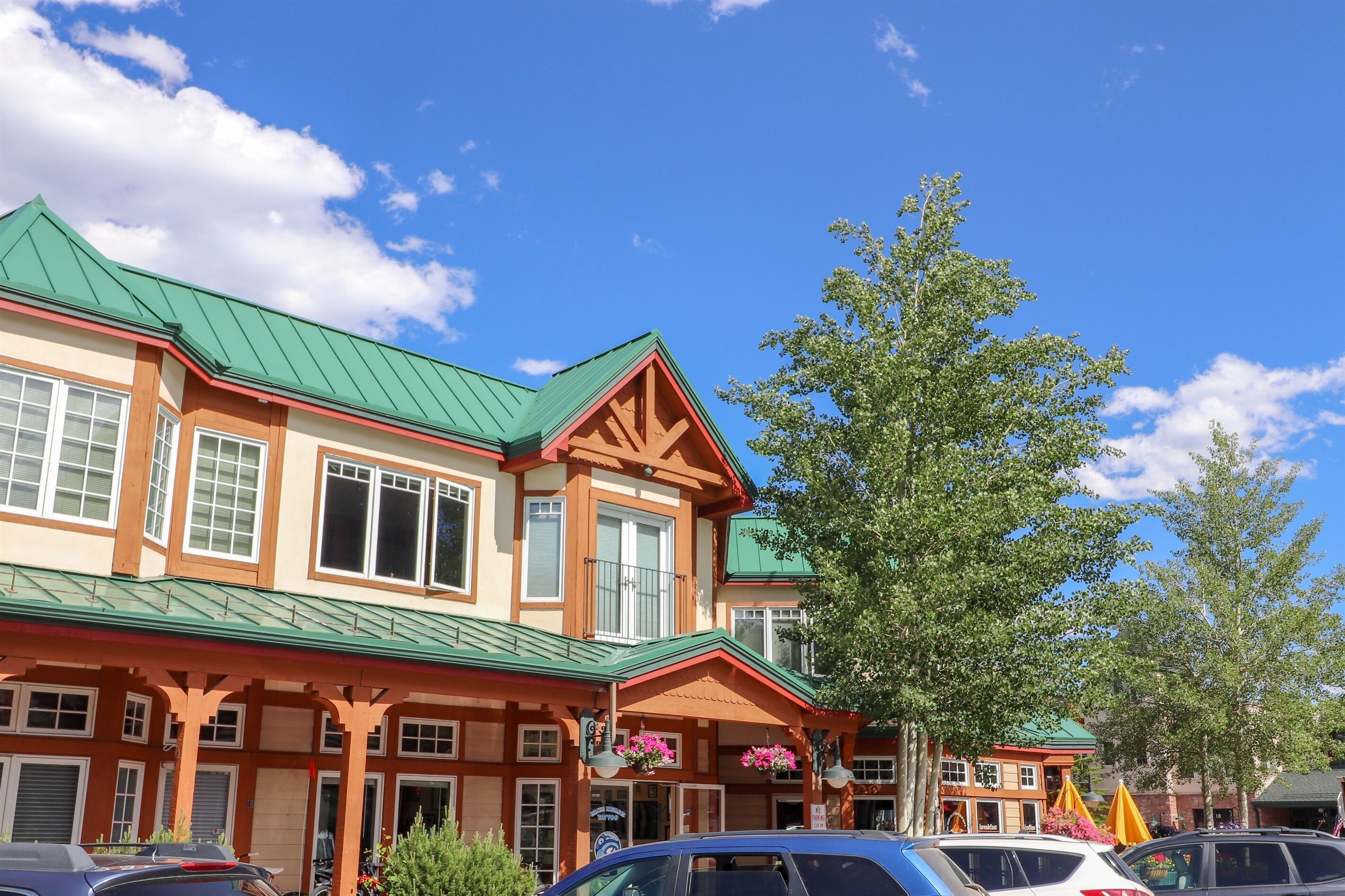A multi-story building with a green roof, large windows, and a covered entrance area with hanging flower baskets.