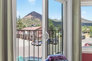 A view through a window with a mountain in the background, a parking lot with cars, and a building with a sign.