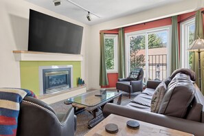A living room with a fireplace, a sofa, a television, and a window with curtains.