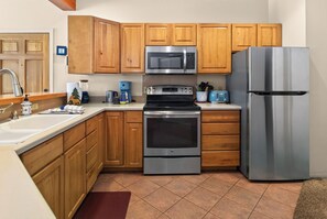 Cocina con armarios de madera, un refrigerador de acero inoxidable, microondas, horno y cafetera.