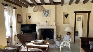 Un salon chaleureux avec une cheminée, des poutres apparentes, un téléviseur et des sièges confortables.