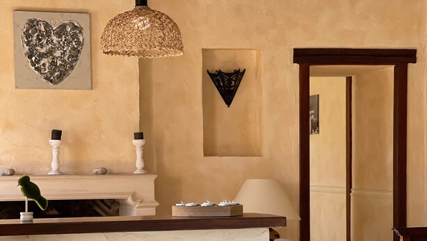 Une cuisine rustique avec une table en bois, des chaises blanches, un luminaire suspendu et un élément décoratif mural.
