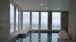 Une piscine intérieure moderne, dotée de grandes baies vitrées et offrant une vue sur la mer.