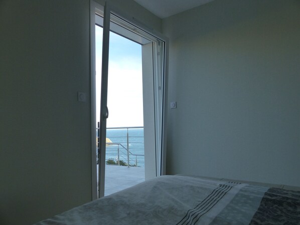 Une chambre à coucher avec un lit, une vue sur la mer par une porte ouverte et un balcon avec une balustrade.