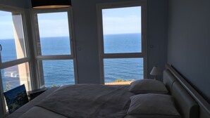 Une chambre avec un grand lit, deux fenêtres et une vue sur la mer.