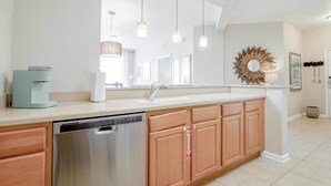 A modern kitchen with a dishwasher, wooden cabinets, a large mirror, pendant lights, and a decorative wall piece.