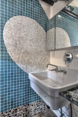 Kylpyhuone, jossa on valkoinen pesuallas, peili ja sinisistä mosaiikkilaatoista tehty seinä.