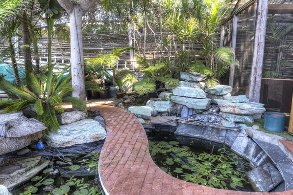 A garden with a curved brick pathway, a pond with lily pads, and various tropical plants.