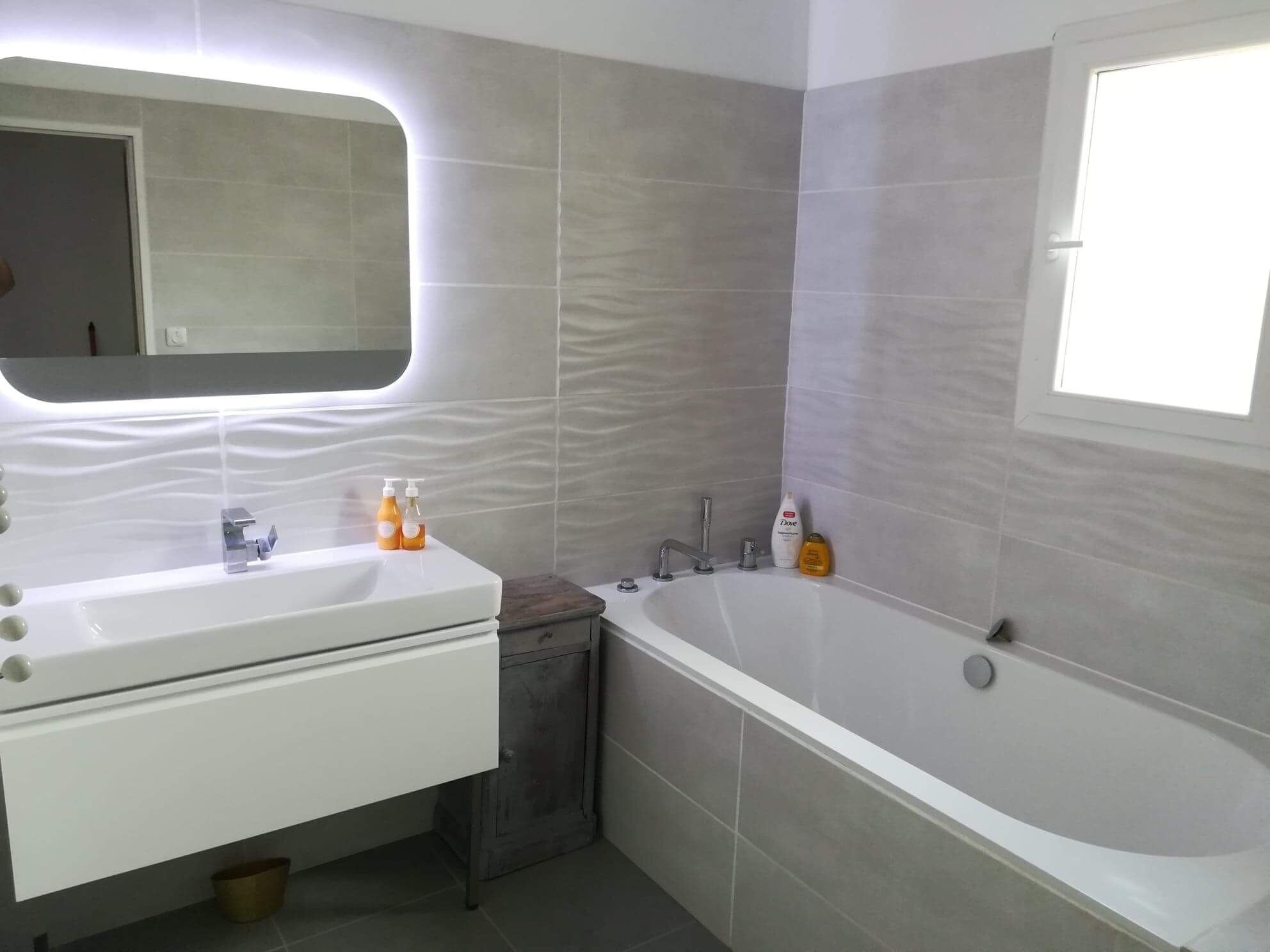 Une salle de bain moderne dotée d’un meuble-lavabo à deux vasques, d’une grande baignoire et d’un miroir au design ondulé original.