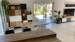 Een moderne woonkamer met een houten eettafel, witte stoelen, een ingebouwde televisie en een boekenkast.