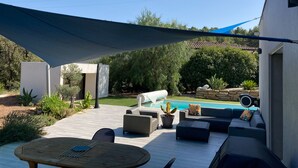 Een terras met buitenmeubilair, een zwembad en een groot zonnescherm.