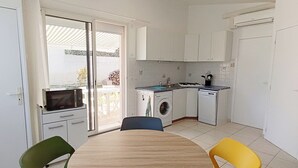 A compact kitchen with a microwave, washing machine, and dishwasher. There is a dining table with chairs and a sliding glass door leading to an outdoor area. - GITE FOR 4 PERS WITH POOL (Agde)