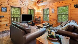 L’intérieur d’une cabane avec des murs en bois, un canapé en cuir, un téléviseur et une bibliothèque.