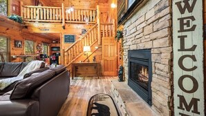 L’intérieur chaleureux d’un chalet avec un escalier en bois, une cheminée et une pancarte indiquant « BIENVENUE ».