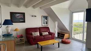 A modern living room with a red leather sofa, a yellow coffee table, and a large window offering a view of the sea. - PIRIAC SUR MER Large T2 full SEA FACE Terrace WIFI broadband (Piriac-Sur-Mer)