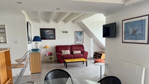 A modern living room with a glass dining table, red leather sofa, and a TV mounted on the wall. - PIRIAC SUR MER Large T2 full SEA FACE Terrace WIFI broadband (Piriac-Sur-Mer)