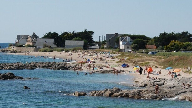 A beach with rocky shoreline, people sunbathing, and buildings in the background. - PIRIAC SUR MER Large T2 full SEA FACE Terrace WIFI broadband (Piriac-Sur-Mer)