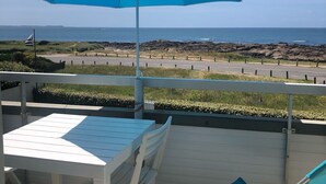 A terrace with a table and chairs, a blue umbrella, and a view of the ocean and rocky coastline. - PIRIAC SUR MER Large T2 full SEA FACE Terrace WIFI broadband (Piriac-Sur-Mer)