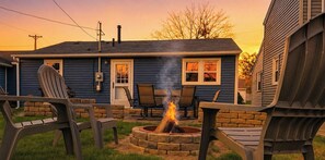 A house with a fire pit in the backyard, outdoor seating, and a clear sky.