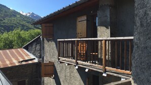 Una cabaña rústica de montaña con balcón, paredes de piedra y vistas a montañas nevadas.