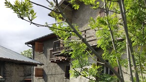 Un edificio rústico con balcón, un pequeño jardín y una pila de leña.