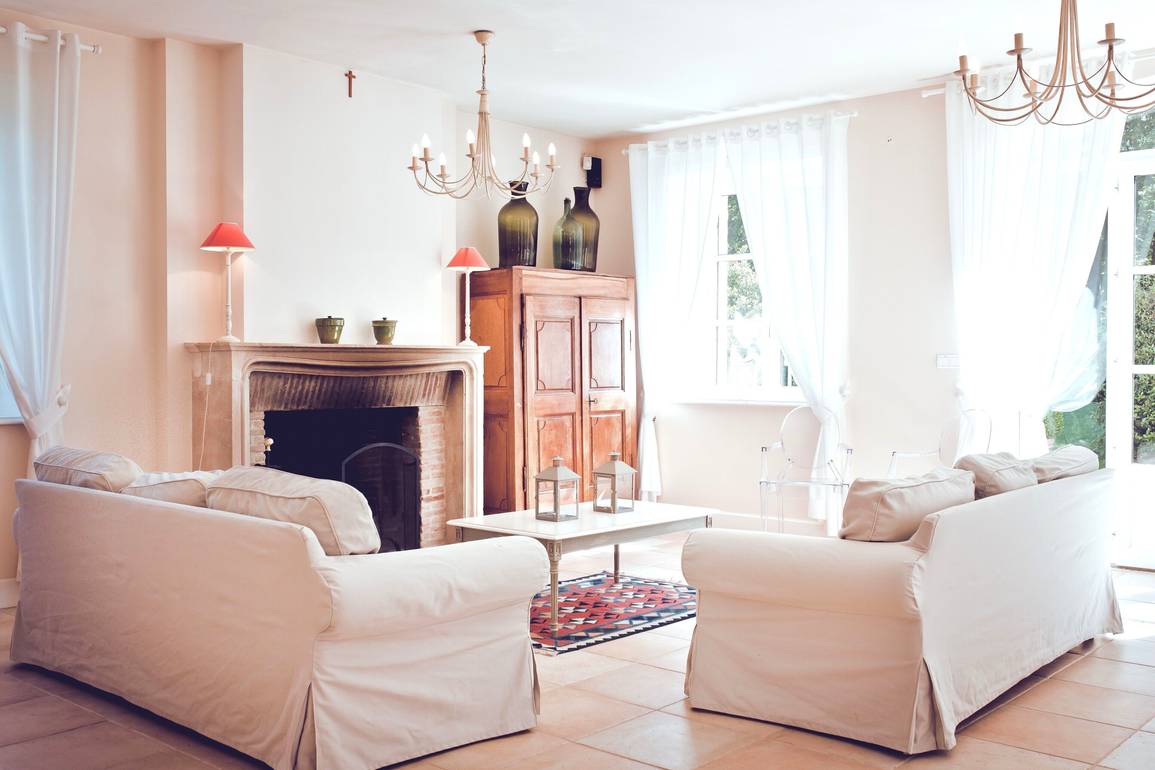 A living room with two white sofas, a fireplace, a chandelier, and a view of greenery outside.