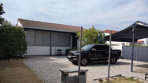 A black SUV parked in a gravel driveway with a covered carport and a building with a tiled roof in the background. - LARGE PRIVATE COURT HOUSE CLOSED (Saint Palais sur Mer)