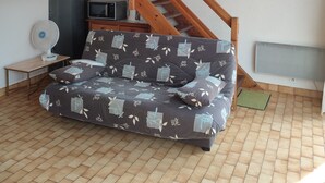 A room with a wooden staircase, a sofa with patterned cushions, a standing fan, a television, and a framed picture on the wall. - LARGE PRIVATE COURT HOUSE CLOSED (Saint Palais sur Mer)