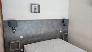 A hotel room with a grey headboard, a bed with a white mattress, a small shelf with a decorative item, and two wall-mounted lamps. - LARGE PRIVATE COURT HOUSE CLOSED (Saint Palais sur Mer)