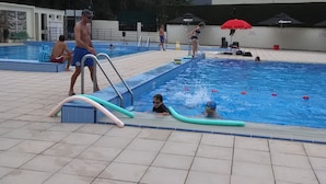 Un área de piscina con suelo de baldosas, un trampolín y un puesto de salvavidas.