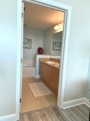 A bathroom with a bathtub, two sinks, wooden cabinets, and a rug. - 🏖️Aqua 1410 Oceanfront; King/Dbl beds,  2 full baths (Panama City Beach)