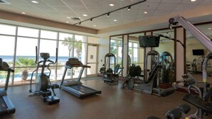 A gym with treadmills, elliptical machines, and weight equipment, large windows with a view of the ocean.