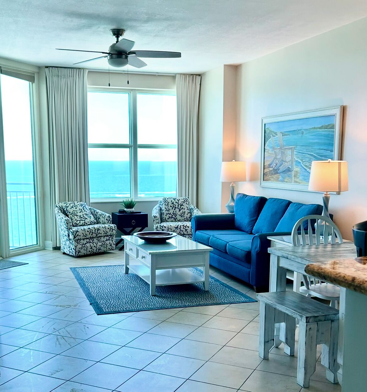 A living room with a blue sofa, patterned armchairs, a coffee table, and a ceiling fan.