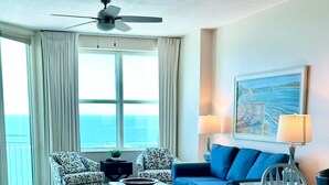 A living room with a blue sofa, patterned armchairs, a coffee table, and a ceiling fan.